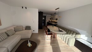 A modern living room with a sofa, a dining table, and a kitchen in the background. - Waterfront apartment w/ beach access & balcony (Knokke-Heist)