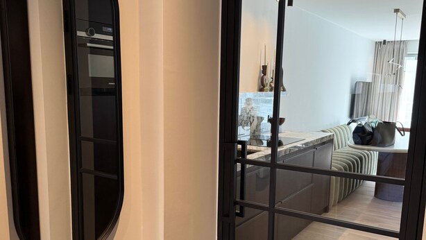A modern interior with a sliding glass door leading to a balcony, a round mirror on the wall, and a glimpse of a living area with a sofa and a table. - Waterfront apartment w/ beach access & balcony (Knokke-Heist)