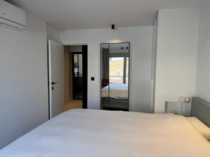 A hotel room with a bed, a door leading to a balcony, and a mirror reflecting the room. - Waterfront apartment w/ beach access & balcony (Knokke-Heist)