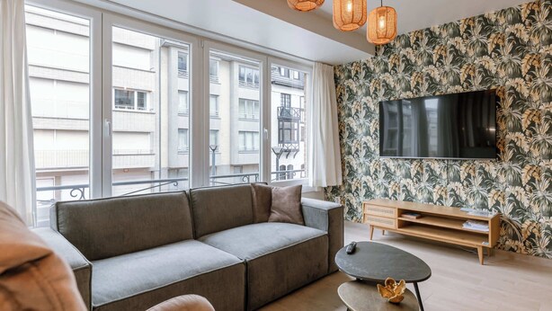 Ein modernes Wohnzimmer mit einer Couch, einem Fernseher und einer Wand mit tropischem Wandpapier.