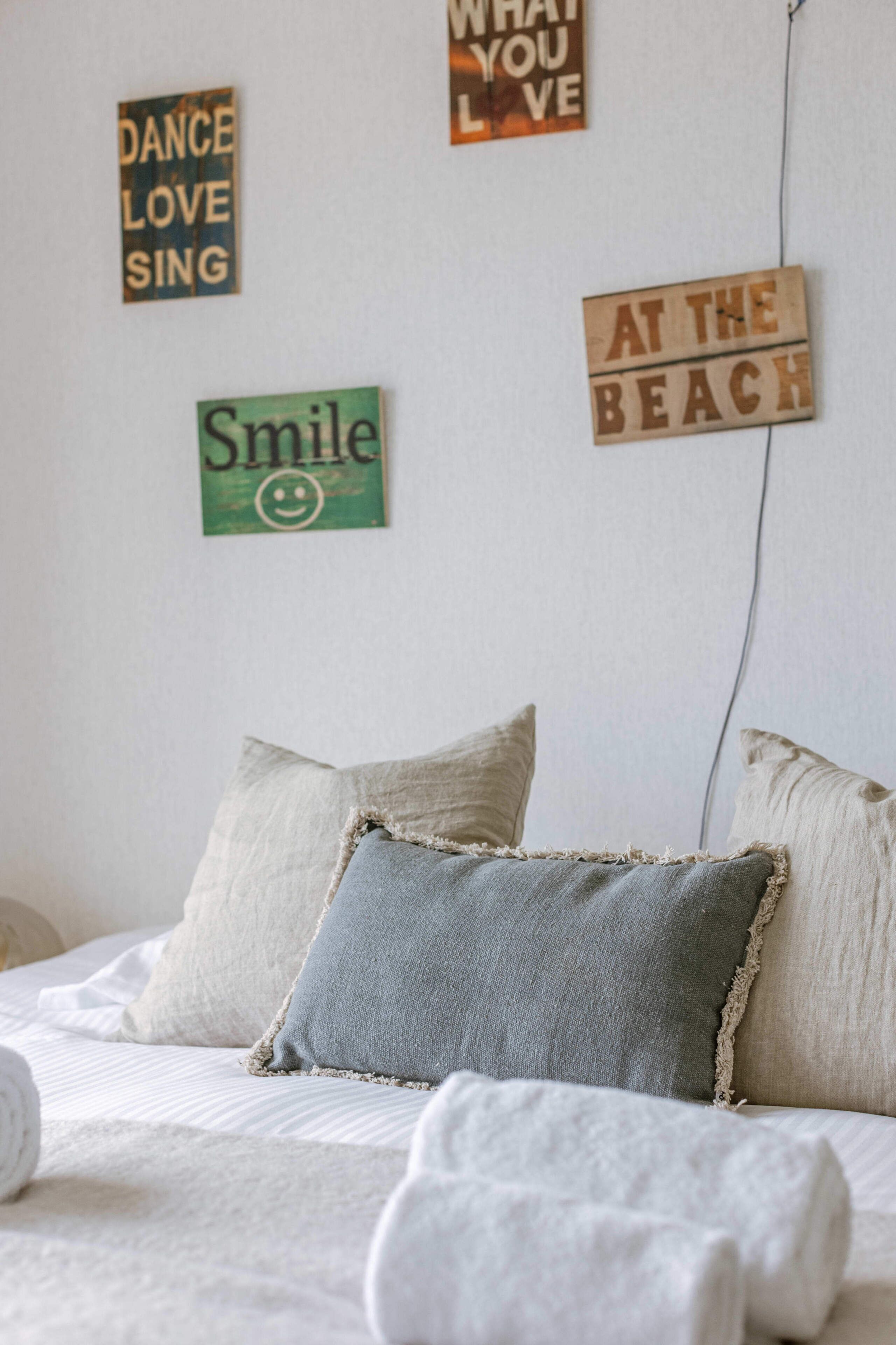 Un dormitorio con cama, almohadas y adornos en la pared, incluyendo letreros con frases como 'What you love' y 'Smile'.