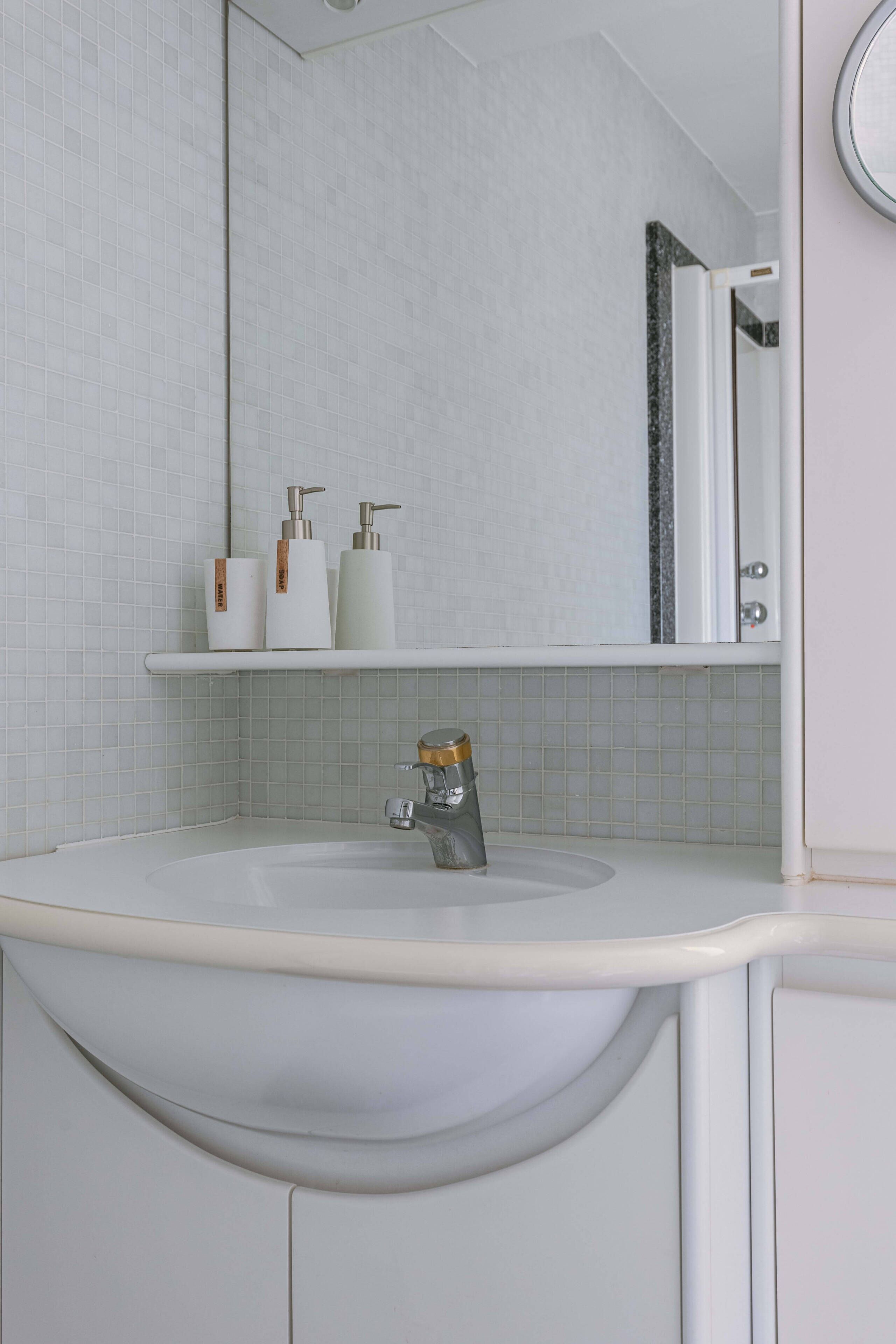 Un baño con un lavamanos blanco, un espejo y un estante con artículos de aseo.