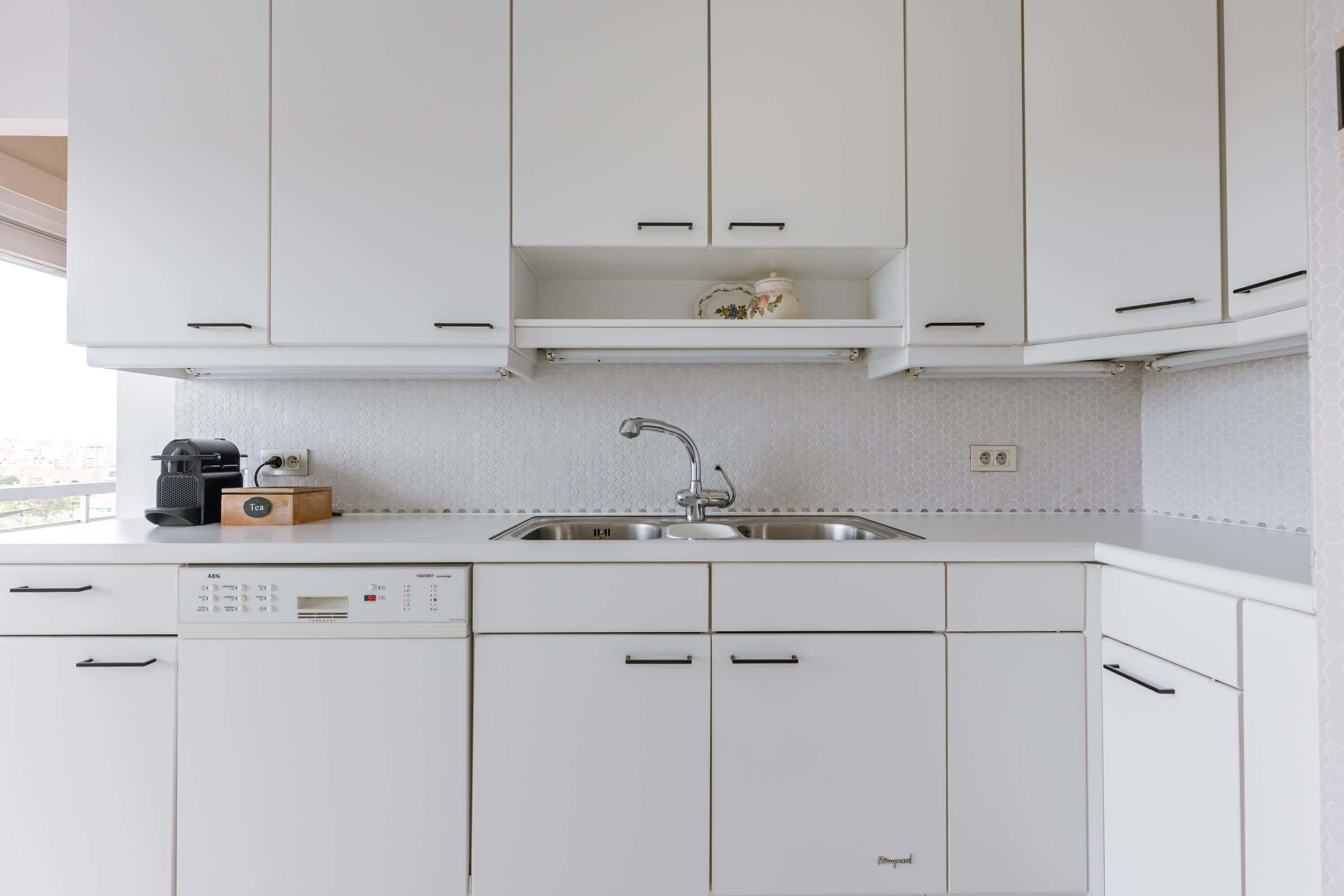 A modern kitchen with white cabinetry, a built-in dishwasher, and a stainless steel sink.