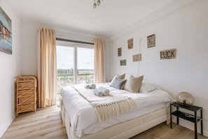 Ein Schlafzimmer mit einem großen Bett, einem Fenster mit Vorhängen, einem Nachttisch mit Lampe und motivierenden Wandbildern.