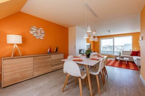 Une cuisine moderne avec un coin repas, des meubles en bois, des chaises blanches et des luminaires suspendus.