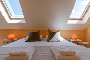 Une chambre d’hôtel avec un lit, deux tables de chevet avec des lampes, une lucarne et des serviettes sur le lit.