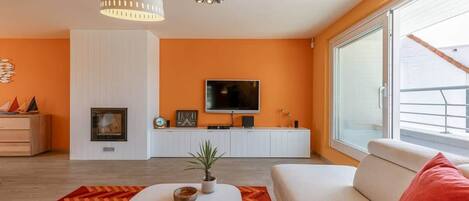 A modern living room with a sofa, a coffee table, a fireplace, a TV, and a large window.