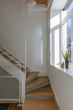Ein modernes Interieur mit einer weißen Treppe, einem Fenster mit Blick und einer kleinen Pflanze am Fensterbrett.