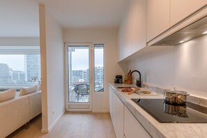 A modern kitchen with a black induction cooktop, white cabinets, and a view of the city through a glass door. - Waterfront apartment w/ balcony & elevator (Oostende)