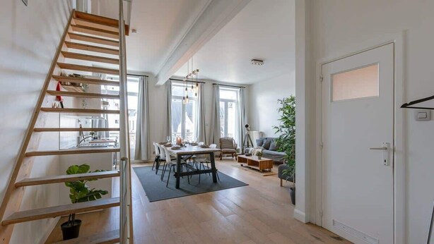 Un amplio salón con una escalera de madera, una mesa de comedor y un ventanal grande.