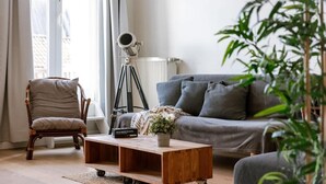 Una sala de estar con un sofá, una silla, una mesita de centro, un telescopio y una planta.
