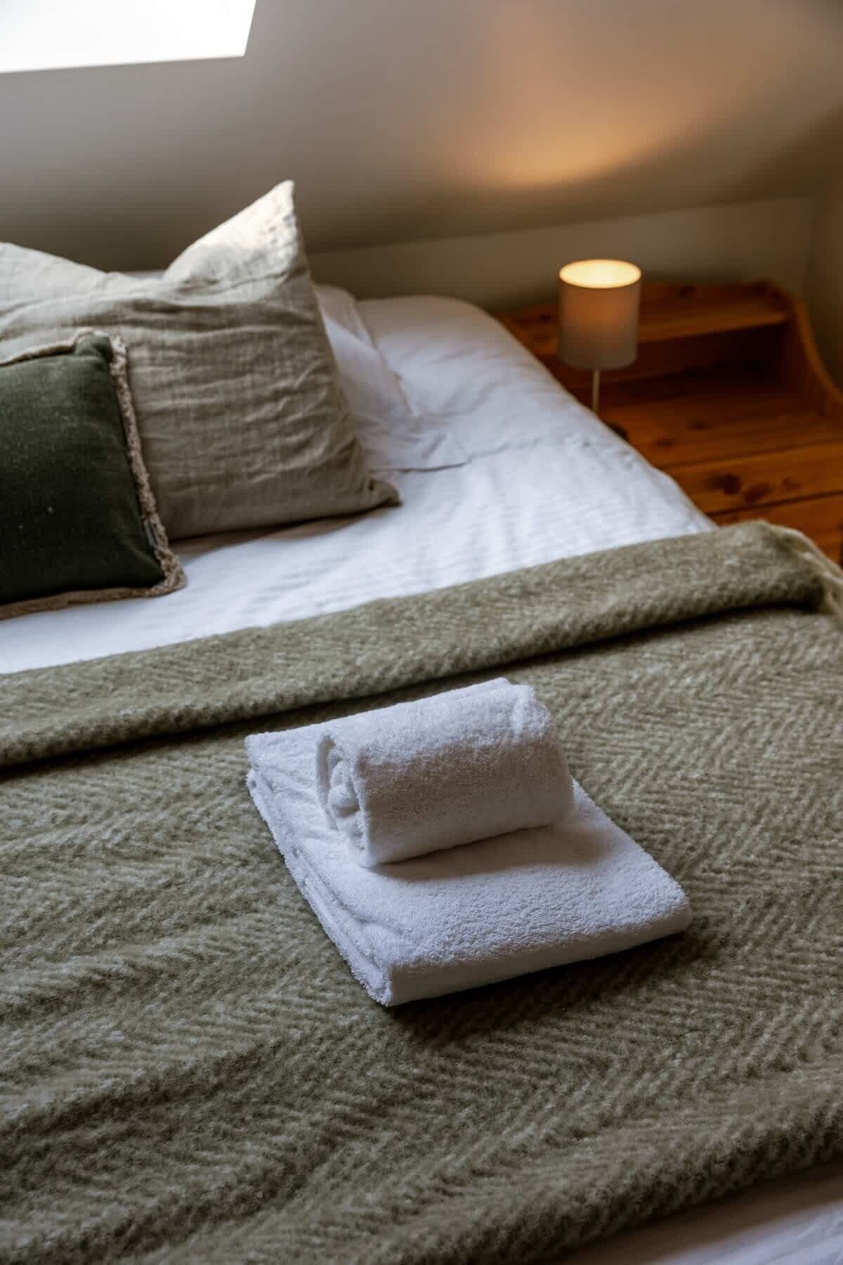 A bed with a green blanket and a folded white towel.