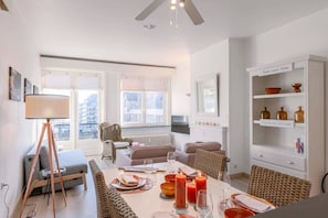 Ein modernes Wohnzimmer mit Essbereich, großen Fenstern und einer weißen Schrankwand.