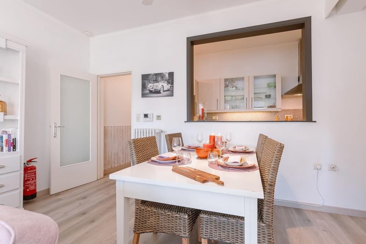 A dining area with a white table, wicker chairs, and a mirror above.