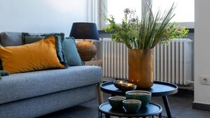 En stue med en grå sofa, et lille bord med en plantevase og en radiator.