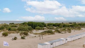 A beachside hotel with a row of rooms, a flag with 'DUINAS' on it, and a sandy beach with dunes in the background. - Coastal getaway w/ full kitchen & workspace (Knokke-Heist)