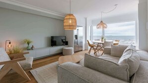A modern living room with a sofa, a coffee table, a TV, and a dining area with chairs. - Coastal getaway w/ full kitchen & workspace (Knokke-Heist)