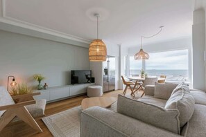 A modern living room with a sofa, a coffee table, a TV, and a dining area with chairs. - Coastal getaway w/ full kitchen & workspace (Knokke-Heist)