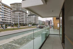Ein modernes Gebäude mit geschwungenen Balkonen, einer Glasumlaufung und Blick auf eine belebte Straße mit Autos und weiteren Gebäuden.