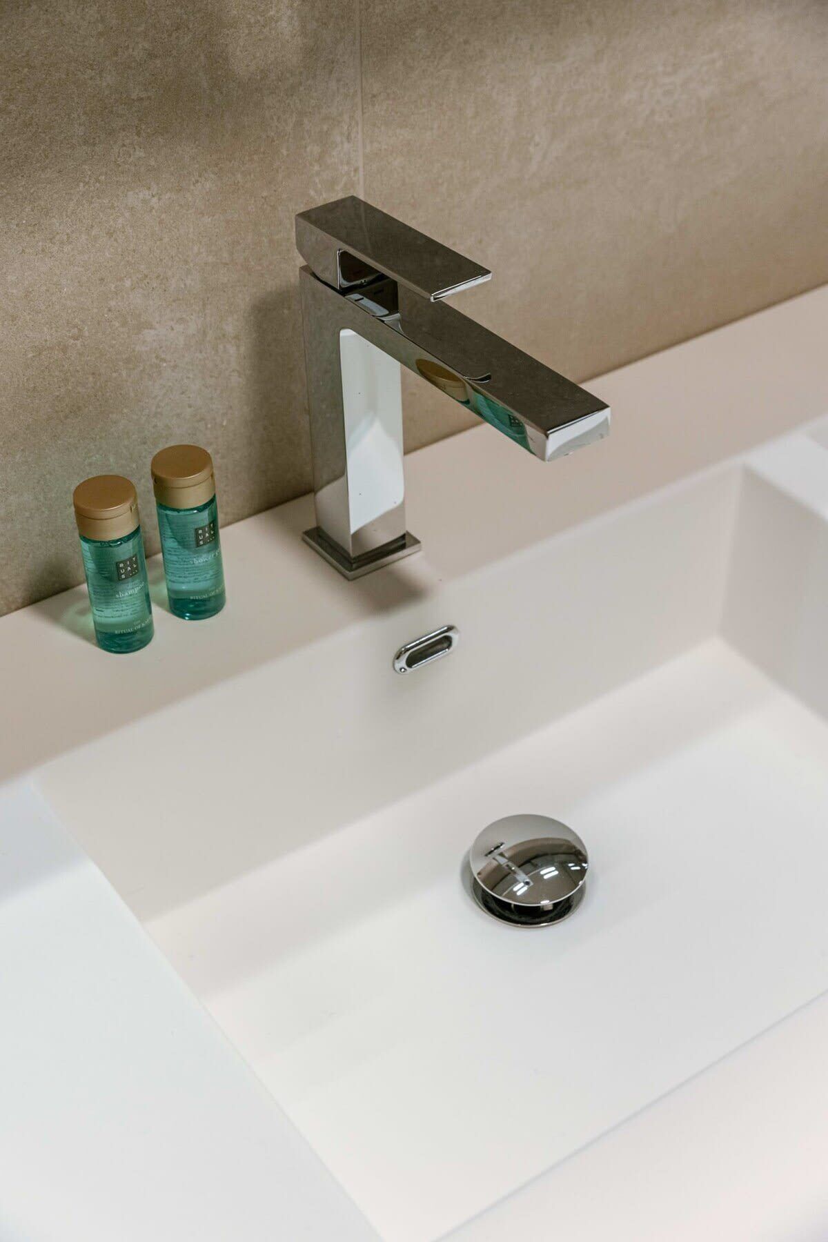 A bathroom with a modern faucet, a white sink, and two bottles of liquid soap.