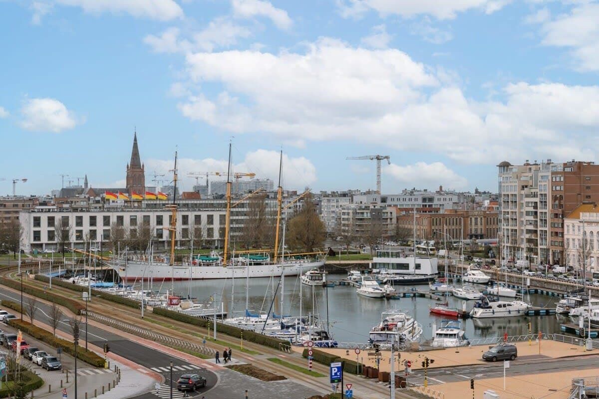 A marina with boats, a church spire, and modern buildings in the background.