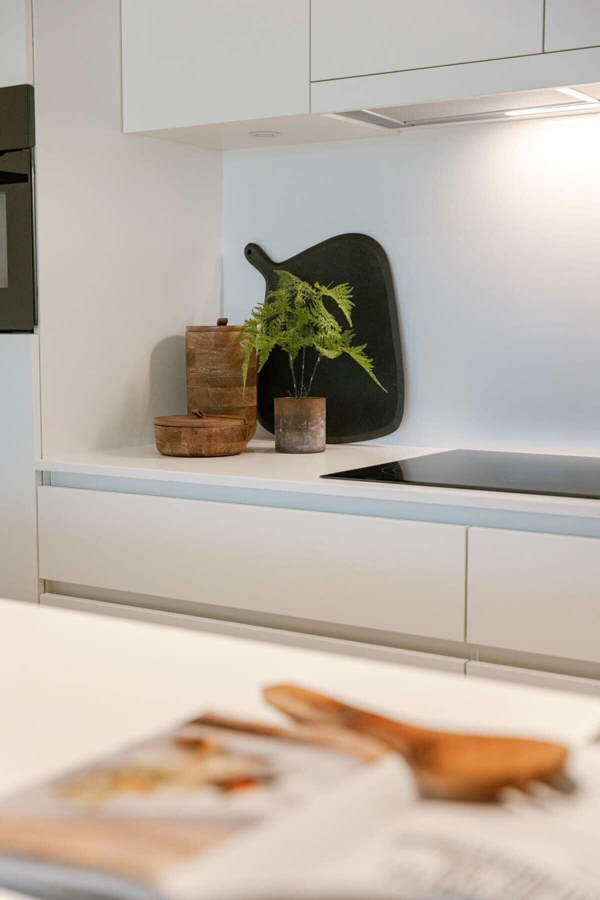 A kitchen with white cabinets, a black cutting board, a wooden bowl, and a potted plant.