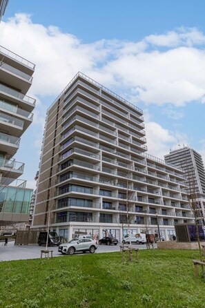 A multi-story building with balconies, a parking area, and a grassy foreground. - Waterfront apartment w/ balcony & parking (Oostende)