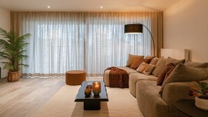 Ein Wohnzimmer mit einer Couch, einem Couchtisch, einer Stehlampe und einem großen Fenster mit Vorhängen.