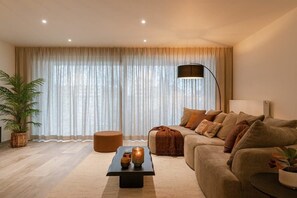 A living room with a sofa, a coffee table, a floor lamp, and a large window with curtains. - Waterfront apartment w/ balcony & parking (Oostende)