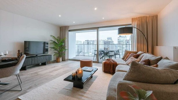 Ein modernes Wohnzimmer mit großem Fenster, Flachbildfernseher, einer Couch, einem Couchtisch und einem Essbereich.