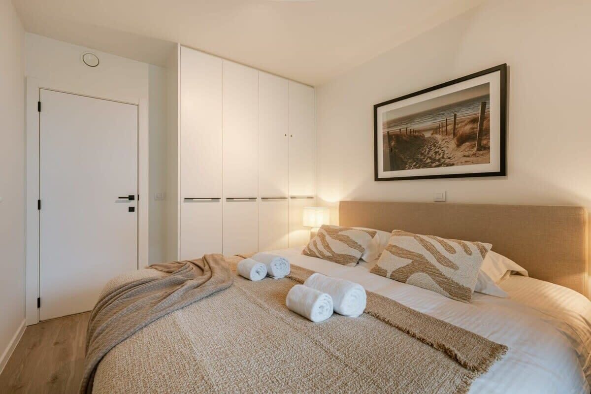 Un dormitorio con cama, armario, un cuadro enmarcado en la pared y una puerta.