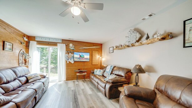 Ett vardagsrum med lädersoffor, en takfläkt, en tv och en skylt med texten ”Beach House”.