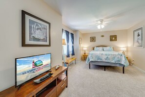 A bedroom with a bed, a TV, a ceiling fan, and artwork on the walls. - Island Bay Dreams by Seaside Vacations & Sales (Chincoteague Island)