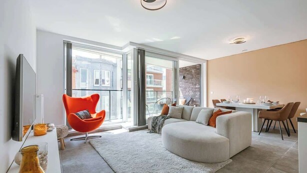 Een moderne woonkamer met een bank, een rode fauteuil, een eettafel met stoelen en een televisie.