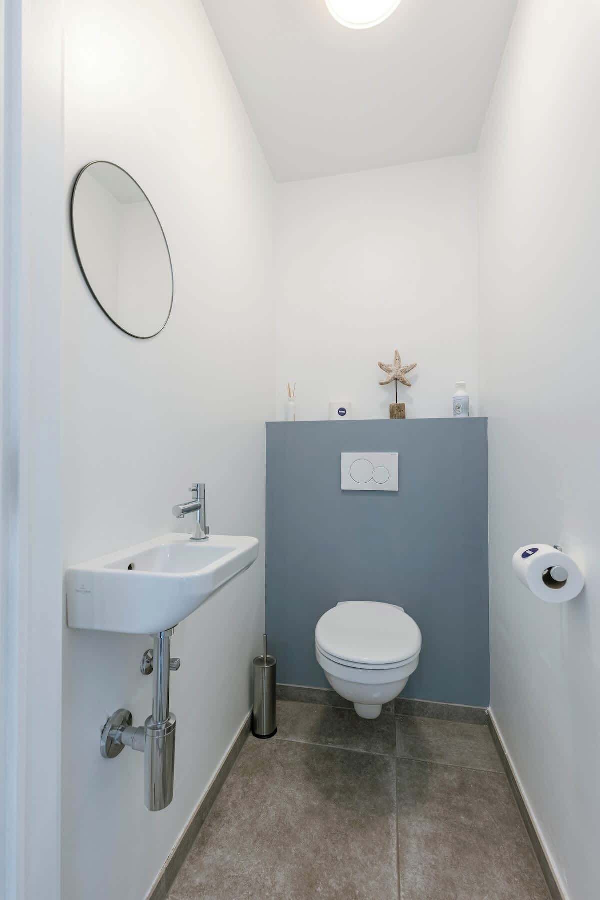 A small, modern bathroom with a white sink, a toilet, and a mirror.