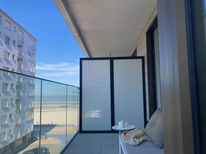 A balcony with a glass railing, a small round table, and a sofa with cushions. - Bright 1BR apartment w/ sea-view (Oostende)