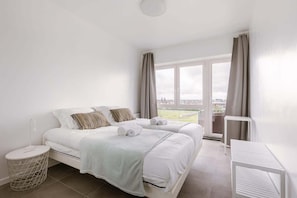 Ein Hotelzimmer mit zwei Betten, Blick auf die Stadt und einem Balkon mit Vorhängen.
