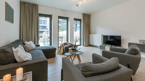 Ein modernes Wohnzimmer mit einer Couch, Sesseln, einem Fernseher und einem kleinen Tisch.
