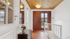 Ein Korridor mit Holzboden, weißen Wänden, einer Holztür, einem weißen Geländer und einem gefliesten Boden.