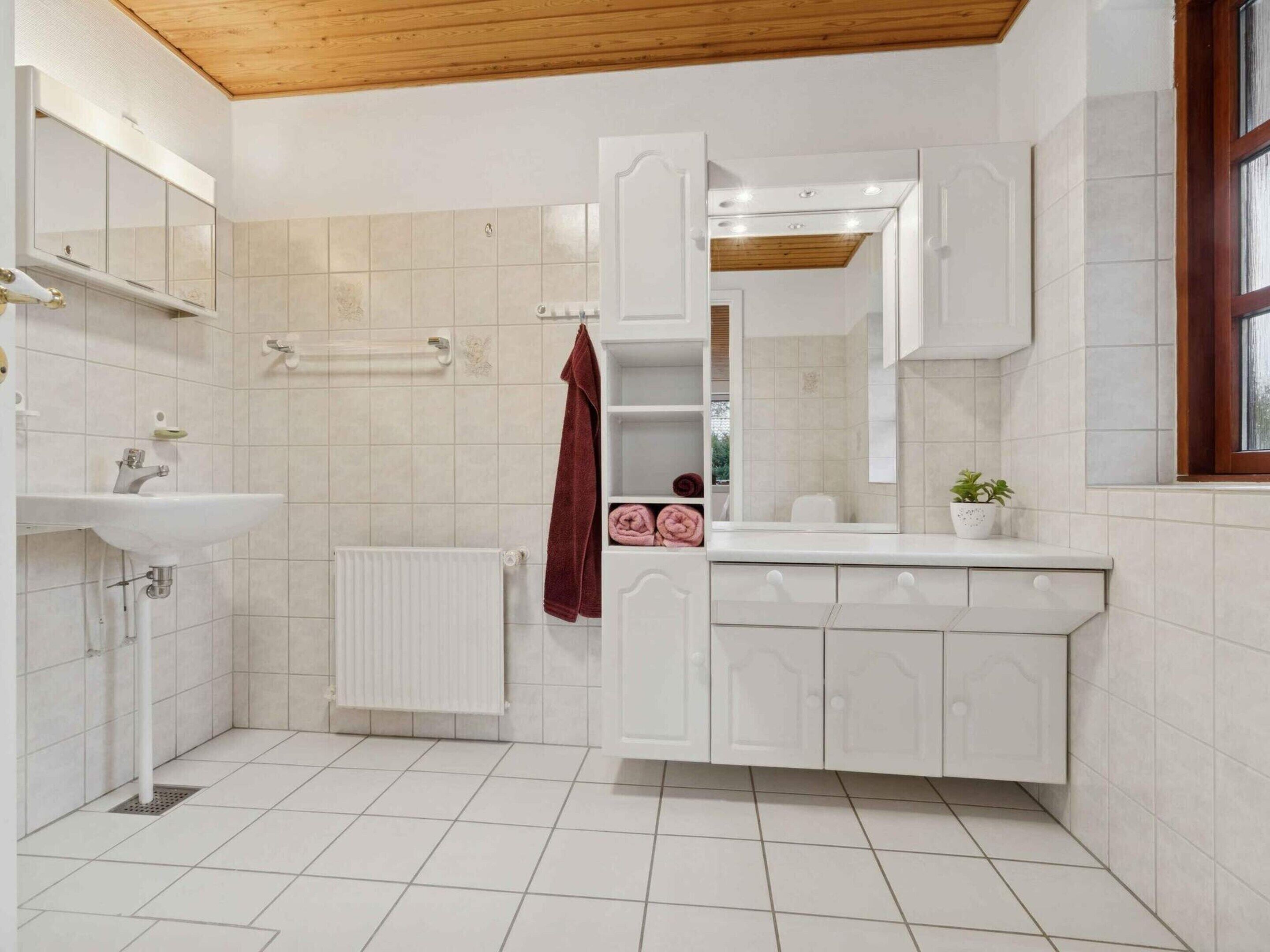 Ein Badezimmer mit weißem Waschbecken, Spiegel, Handtuchhalter und Heizkörper.