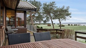 Eine Holzterrasse mit Tisch und Stühlen, mit Blick auf einen See, Bäume und eine Rasenfläche.