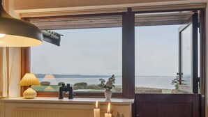 Ein Zimmer mit Seeblick, ein Tisch mit Kerze, eine Lampe, Fernglas und eine Vase mit Blumen.