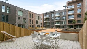 Un patio con una mesa y sillas, una cerca de madera y un edificio de varios pisos con balcones.