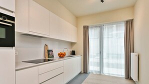 Una cocina moderna con armarios blancos, encimera negra y ventana con cortinas de gasa.