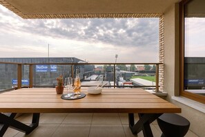 Un balcón con mesa de madera, planta en maceta y copas de vino.