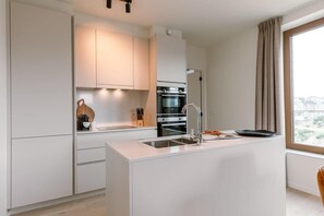 Une cuisine moderne avec des meubles blancs, un îlot central doté d’un évier et une grande fenêtre offrant une belle vue.