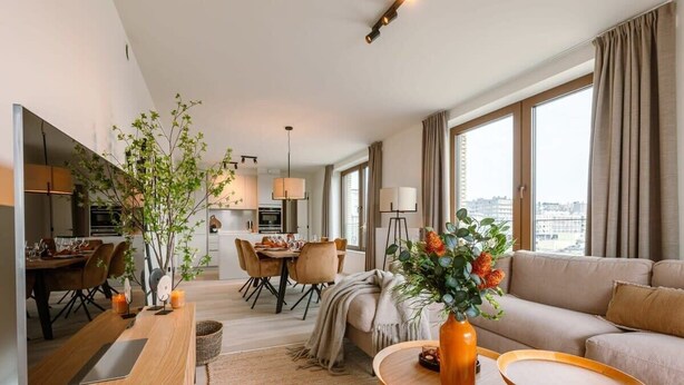 En moderne stue med sofa, spiseområde og køkken i baggrunden.