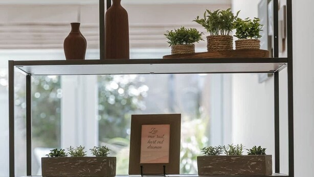 Une étagère métallique à plusieurs niveaux, ornée de plantes en pot et d’une citation encadrée.