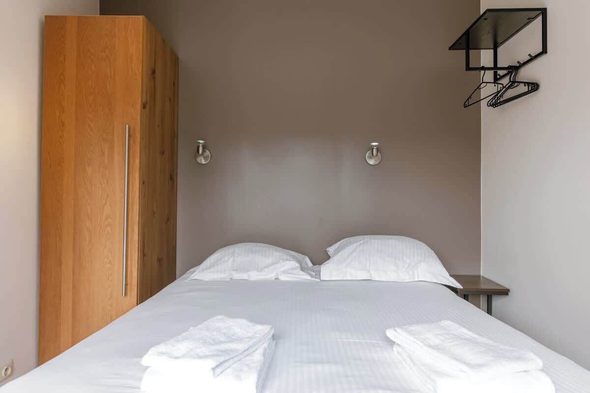 A bedroom with a bed, a wooden wardrobe, and a wall-mounted coat rack.