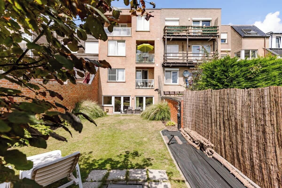 A residential building with a brick facade, multiple balconies, and a grassy backyard.